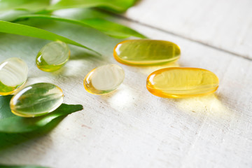 Natural vitamins supplement on white wood background with green leaves.