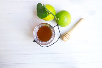 Close up honey jar with lime and honey scoop on wooden background.