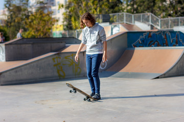 Girl teenager rides on a skateboard. Beautiful fashionable skateboarder in jeans and a hoodie on a ramp.