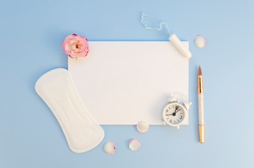 Top view mockup empty paper blank list framed with Women's Period stuff: female pad and tampon. Flat lay with alarm clock and pen on a pastel blue background