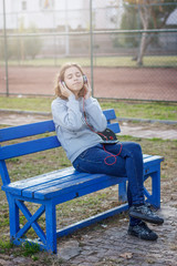 Obraz premium Young beautiful fashionable teenager girl listens to music on headphones from a smartphone
