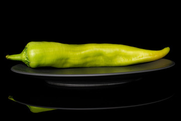 One whole hot green pepper banana on gray ceramic plate isolated on black glass