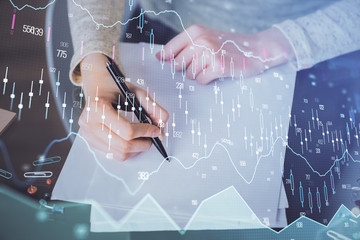 Hand taking notes in notepad. Forex chart holograms in front. Concept of research. Multi exposure