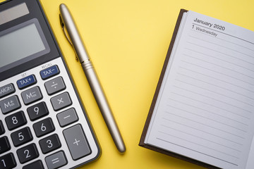 A 2020 business planner concept with calculator, gold pen, 2020 planner and brown paper note