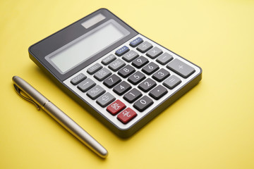 A calculator and gold pen on yellow background  