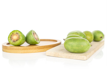 Group of five whole two halves of hardy green kiwi on round bamboo coaster on wooden cutting board isolated on white background
