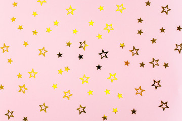 Confetti golden stars on pink background. Holiday backdrop. Flat lay, top view
