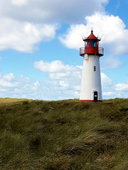 Fototapeta na wymiar Leuchtturm List Ost im Sommer vor blauem Himmel und Wolken mit grünem Gras im Vordergrund