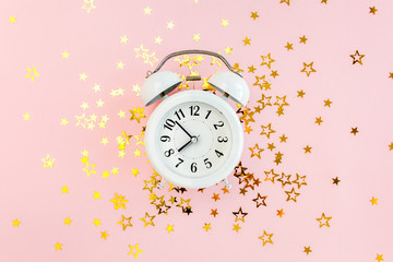 Round frame, alarm clock  covered golden stars confetti, glitter decoration on a pink, festive background. Christmas or New Year pattern. Flat lay, top view