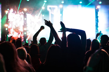 Audience with hands raised at a music festival and lights streaming down from above the stage. Soft...