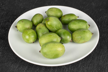 Lot of whole hardy green kiwi on white ceramic plate on grey stone