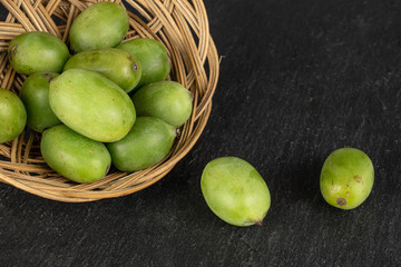 Lot of whole hardy green kiwi in round rattan bowl on grey stone