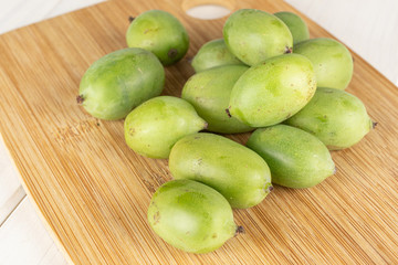 Lot of whole hardy green kiwi on bamboo cutting board on white wood