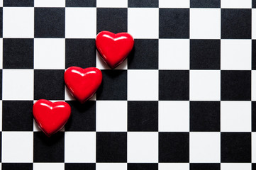 three red hearts lying on black and white chessboard like love concept 
