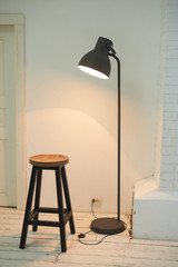 Minimalism. A stool and a loft-style lamp against a white wall.