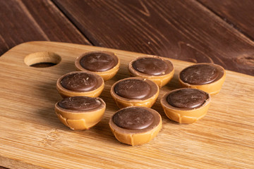 Group of eight whole sweet brown toffee on bamboo cutting board on brown wood