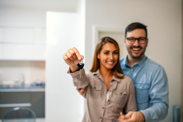 Shot of a cheerful young couple holding a key together to their new home while standing inside during the day. Couple holding the keys to their new house. Moving house concept