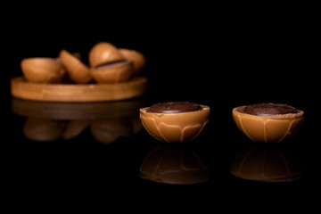 Lot of whole sweet brown toffee on round bamboo coaster isolated on black glass