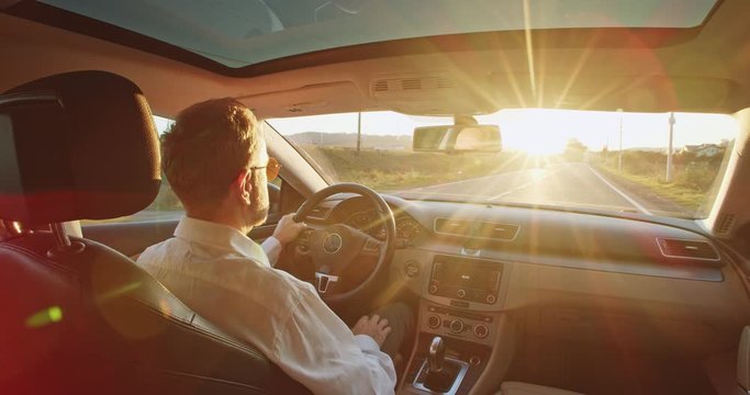 Rear view of classic style adult business man in sunglasses driving car with amazing sunlight rising in front of the road. Freelance traveling. Urban lifestyle. Navigation. Map. Driver dreaming.
