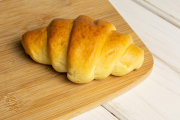One whole sweet golden mini croissant on bamboo cutting board on white wood