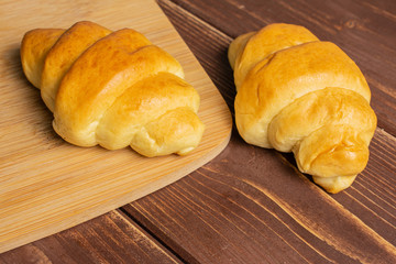 Group of two whole sweet golden mini croissant on bamboo cutting board on brown wood