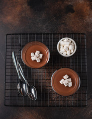 two glasses of panna cotta, decorated with marshmallows. brown textured background, top view, close-up
