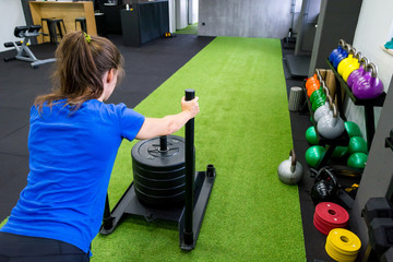 Young female fitness trainer performing sled push in local gym.