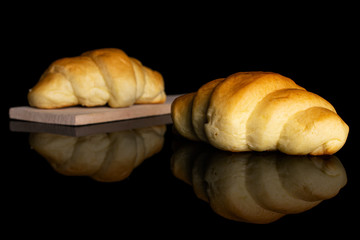 Group of two whole sweet golden mini croissant on small wooden cutting board isolated on black glass