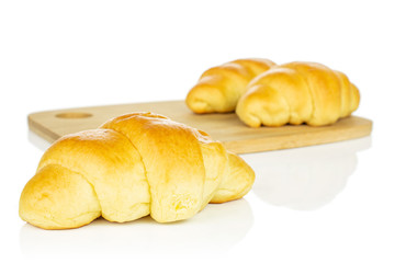 Group of three whole sweet golden mini croissant on bamboo cutting board isolated on white background