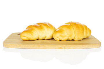 Group of two whole sweet golden mini croissant on bamboo cutting board isolated on white background