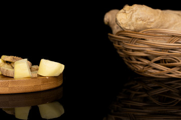 Group of lot of whole three slices two pieces of fresh brown ginger in round rattan bowl on round bamboo coaster isolated on black glass