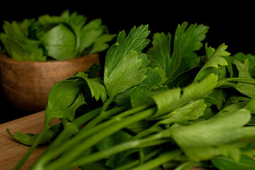Lot of whole lot of pieces of fresh green parsley in bamboo bowl on bamboo cutting board isolated on black glass