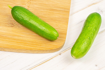 Group of two whole fresh green baby cucumber on bamboo cutting board on white wood