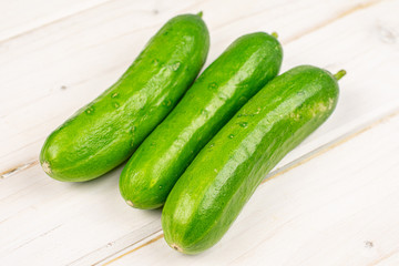 Group of three whole fresh green baby cucumber on white wood