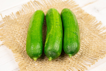 Group of three whole fresh green baby cucumber on natural sackcloth on white wood