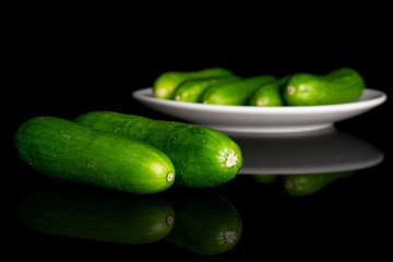 Group of seven whole fresh green baby cucumber on white ceramic plate isolated on black glass