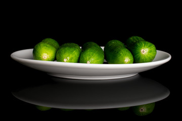Group of five whole fresh green baby cucumber on white ceramic plate isolated on black glass