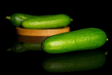Group of three whole fresh green baby cucumber on bamboo coaster isolated on black glass