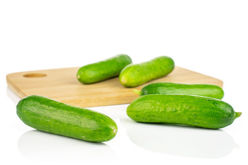 Group of five whole fresh green baby cucumber on bamboo cutting board isolated on white background