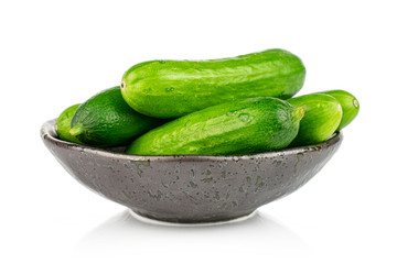Lot of whole fresh green baby cucumber in dark ceramic bowl isolated on white background