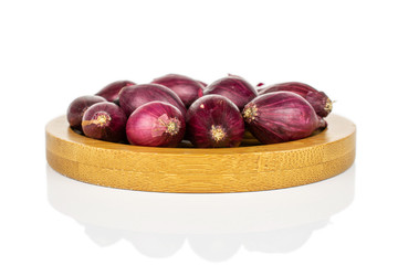 Lot of whole small red onion bulb on bamboo coaster isolated on white background