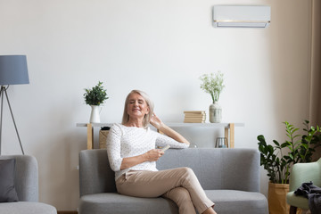 Aged woman sitting on couch holding remote control uses airconditioner