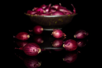 Lot of whole small red onion bulb in dark ceramic bowl isolated on black glass