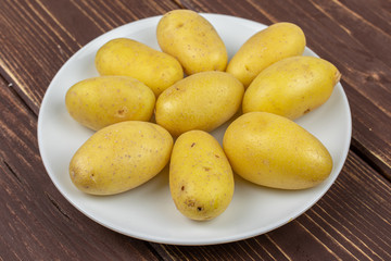 Lot of whole pale yellow potato on white ceramic plate on brown wood