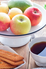 Fresh apples in an enameled stand on a wooden table and breakfast, selective focus