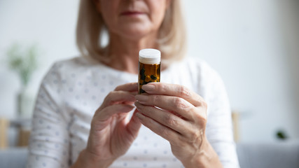 Closeup focus on elderly woman hands holding bottle of pills