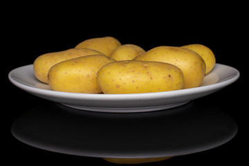 Lot of whole pale yellow potato on white ceramic plate isolated on black glass