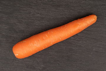 One whole fresh orange carrot flatlay on grey stone