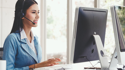 Customer support agent or call center with headset works on desktop computer while supporting the...