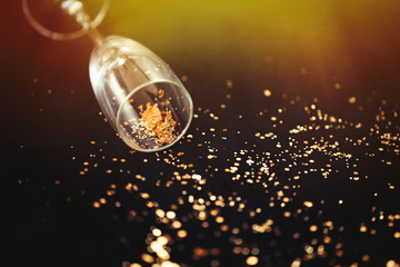 One glass of champagne with golden sparkles inside on black background, selected focus, New Year and Christmas holidays background.